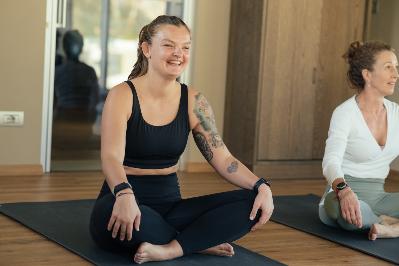 Zwei Frauen sitzen entspannt und lächelnd auf Yogamatten bei beyond – Wohlbefinden und Verbindung zum eigenen Körper.