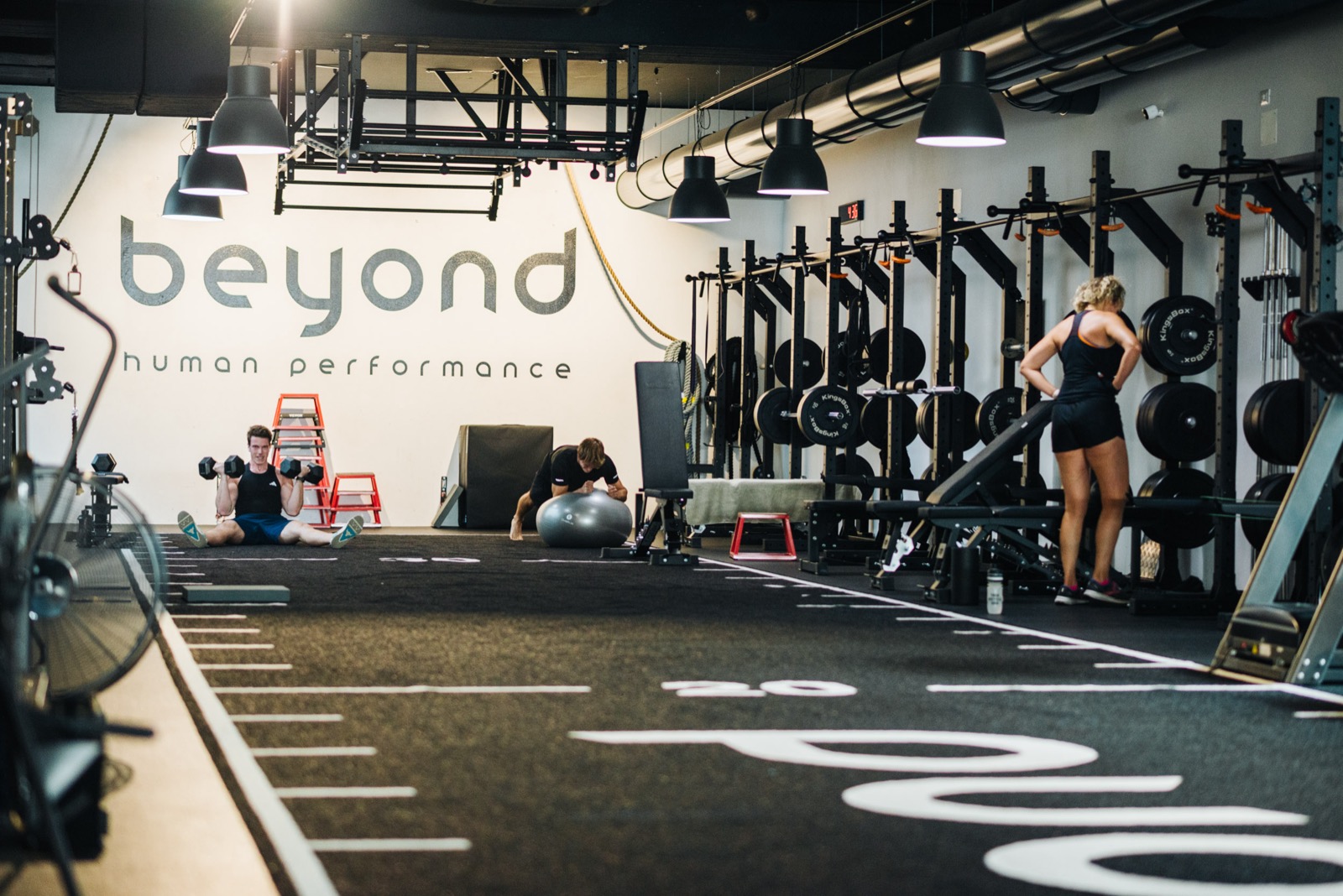 Open-Gym-Fläche bei beyond mit freien Gewichten, im Hintergrund trainieren zwei Personen eigenständig.